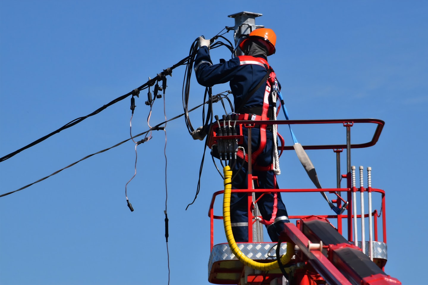 Elektriker im orangefarbenen Helm arbeitet von einer Hebebühne aus an Kabeln.
